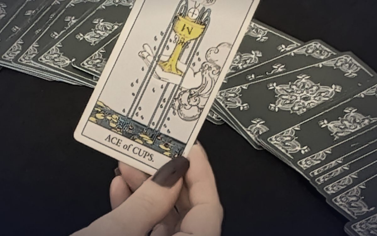 Hand hält die Tarotkarte Ass der Kelche